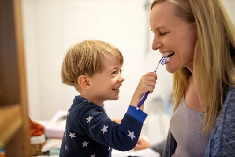 little boy brushing teeth of his mother and smiling.